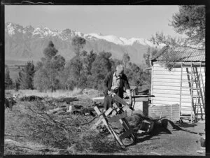 Elderly man sawing wood beside his shack on the shores of Lake Wakatipu, Central Otago