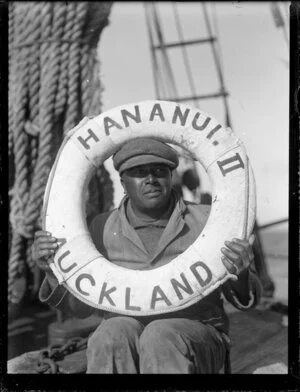 Charlie Jackson sitting on the boat with a lifebelt with the words 'Hananui II Auckland' over his head