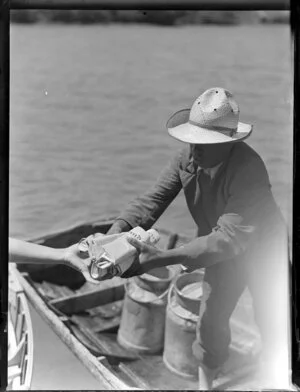 Man in a rowing boat being handed several newspapers, cream launch trip, Bay of Islands