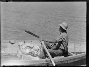 Man in a rowing boat with a parcel, cream launch trip, Bay of Islands
