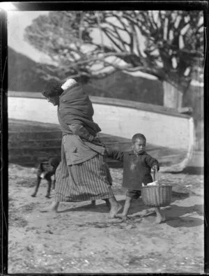 Unidentified woman walking with infant on her back, and small boy following with basket