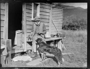 Rural scene with a man, kitten and dog outside a house