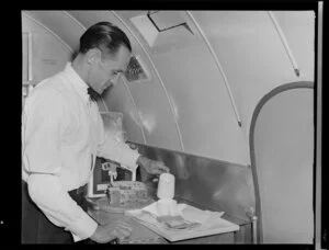 Airline steward F Bennett, in the servery of a Dakota aircraft, assembling a tray of food and drink for a passenger