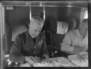 Two men, one in uniform, eating a snack in the cabin of the seaplane Aotearoa