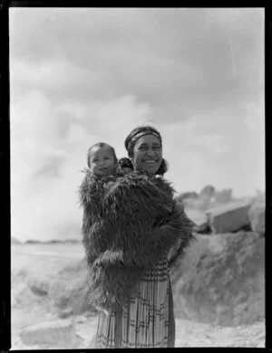 Molly Te Mauri Meihana carrying a young child on her back wrapped in a feather cloak
