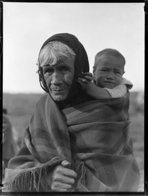 Haehaeora Te Rangitakatu (nee Hurst) carrying a young child, Tiaho Te Waa, on her back wrapped in a blanket