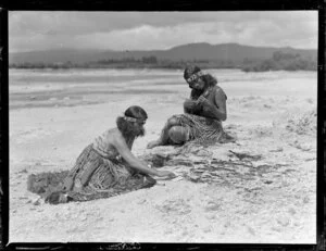A Maori woman playing the ukelele and a Maori woman playing cards on the beach, location unidentified