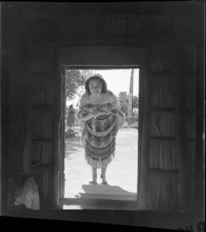 A Māori woman dressed in costume, looking into a whare, Whakarewarewa, Rotorua