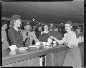 Australian National Airways, flight personnel, Miss Sue Buckland, [Commadore?] V Cerche and Miss Roma Geary, at the refreshment counter, Whenuapai Aerodrome, Auckland
