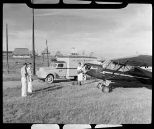 Mr Tom French and an unidentified man, watching a young Fijian man, loading ice cream from a Taylorcraft aeroplane into a Pan American World Airways truck, Nandi Airport, Fiji
