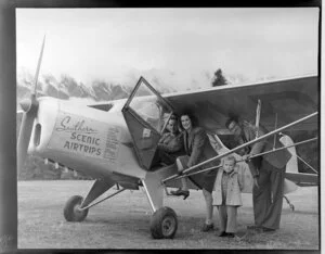 Pilot at the controls of Southern Scenic Airtrips Ltd's Auster J/I Autocrat aeroplane, with an unidentified family group, [Queenstown?]