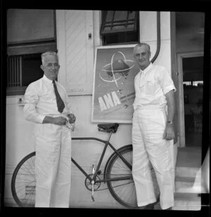 D Butler (left) and C Corbet standing in front of an Australian National Airways poster, Suva, Fiji
