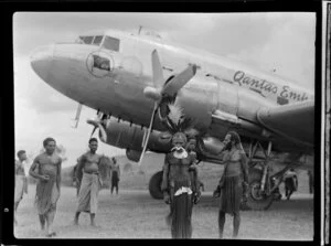 Local people [including chief?] at the arrival of a Qantas Empire Airways flight at Kerowagi airfield, Papua New Guinea, including traditional dress, nose-piercing, and feathered headdress