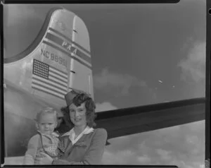 Pan American World Airways stewardess Joyce Halstead holding an unidentified child, having arrived on Douglas DC-4 NC88951 Clipper Racer aircraft [Whenuapai Royal New Zealand Air Force base?]