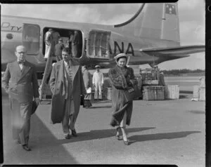 From left, an unidentified man, Sir Laurence Olivier and Vivien Leigh (Lady Olivier) arrive on a Australian National Airways aircraft [Constellation?], while behind them Old Vic Theatre Company luggage is unloaded, Whenuapai Royal New Zealand Air Force base