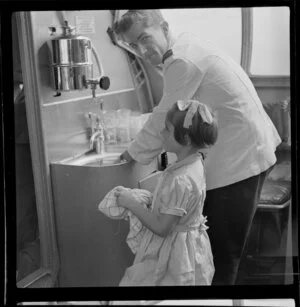 Young child Jennifer Gray, a passenger on Qantas Catalina flying boat service from Suva, Fiji, to Sydney, Australia, helping steward R White with the dishes