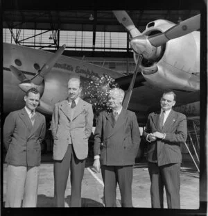 Qantas employees, from left G E Williams (Works Superintendent), N N Roberts (Senior Servicing Constellation), A A Williams (Chief Maintenance Engineer) and D B Hudson (Superintendent Engineering Technical Services), in front of aircraft [Constellation?] in a hangar, Sydney Airport, Mascot, New South Wales, Australia
