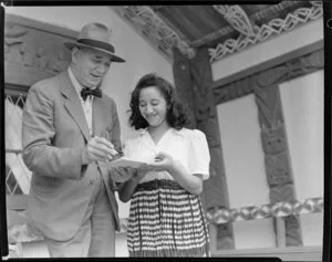 Sir Peter Buck signing autograph book for an unidentified girl at Marae, Ngāruawāhia, Waikato