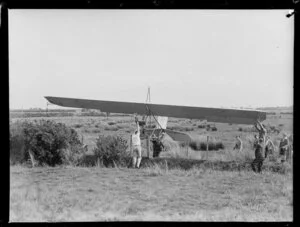 Members of the Auckland Gliding Club lifting a glider over a barbed wire fence in a paddock