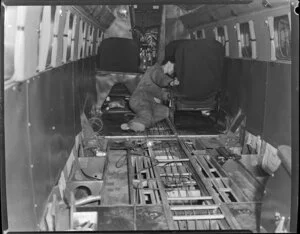 New Zealand National Airways Corporation crew member working on interior of aircraft, in airport hangar, Palmerston North