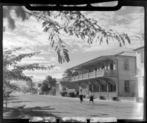 Two Fijians walk down a street past [Northern Hotels?], Lautoka, Fiji