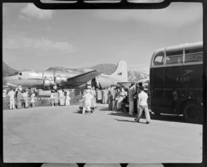 A crowd observes a Qantas Empire Airways Douglas DC-4 (VH-EBK) aircraft at Kowloon, Hong Kong, including a British Overseas Airways Corporation bus in the foreground