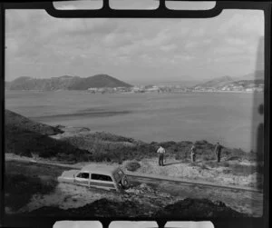 Three men stand beside a [Morris Traveller?] with BOAC insignia overlooking an unidentified bay, Hong Kong