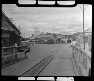 Street in Ba, Fiji, with sugar cane train on railway track on the road, shops, people and vehicles