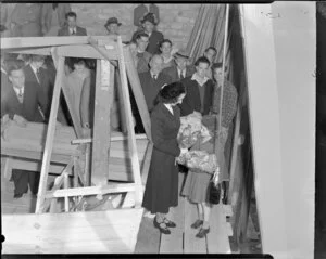 Young girl Margaret McFadden presents [Nora Noverich?], who is about to launch the fishing boat Aorangi (Auckland), with flowers, as a crowd of unidentifed men look on, [Auckland area?]