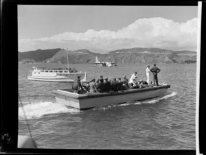 A boat ferries unidentified passengers and Tasman Empire Airways Limited crew to the Short S.45 Solent flying boat, R.M.A Ararangi (ZK-AMM), which is moored in the background, Evans Bay, Wellington