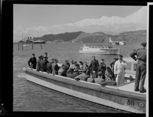 Unidentified passengers and Tasman Empire Airways Limited crew arrive on a boat at the flying boat base near Hataitai Beach, Wellington, with a number of boats, including the Short S.45 Solent flying boat, R.M.A Araragi (ZK-AMM), which is moored in Evans Bay in the background