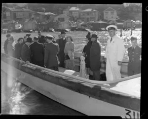 Unidentified passengers and Tasman Empire Airways Limited crew arrive on a boat at the flying boat base near Hataitai Beach, Evans Bay, Wellington, with boat sheds in the background