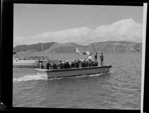A boat ferries unidentified passengers and Tasman Empire Airways Limited crew to the Short S.45 Solent flying boat, R.M.A Ararangi (ZK-AMM), which is moored in the background, Evans Bay, Wellington