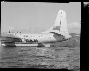 Unidentified passengers and Tasman Empire Airways Limited crew in a small boat alongside the Short S.45 Solent aircraft, R.M.A Araragi (ZK-AMM), Evans Bay, Wellington