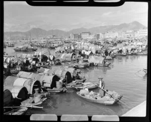 Unidentified man in a boat by village of small houseboats, Hong Kong