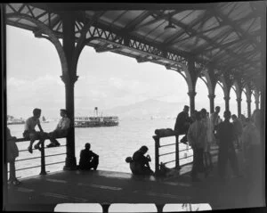 Scene on a pier, with Star Ferry, carrying passengers to Kowloon, on Victoria Harbour in the background