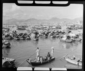An unidentified family of three in a boat amidst a village of small houseboats, Hong Kong