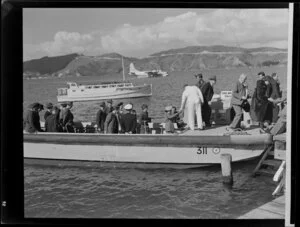Unidentified passengers and Tasman Empire Airways Limited crew arrive in a boat at the flying boat base near Hataitai Beach, Wellington, with the Short S.45 Solent flying boat, R.M.A Araragi (ZK-AMM), moored in Evans Bay in the background