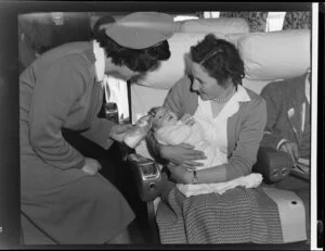 Unidentified air hostess helping a mother and baby on board the DC6, BCPA [British Commonwealth Pacific Airlines]