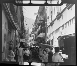 Busy street scene, Hong Kong, including laundry hung across the street and businesses such as Chee Ming & Co Metal Merchants and Cham Ming Tailor