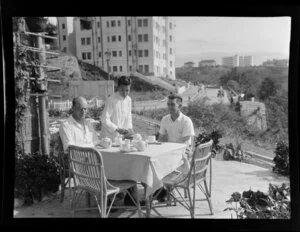 K Gibson and Leo Lemuel White (left to right) take tea on a Hong Kong patio, with an unidentified local waiter serving the two men