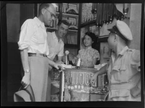 K Gibson and Leo Lemuel White at the counter of a jewellers, Hong Kong, including a British Overseas Airways Corporation driver and shop assistant