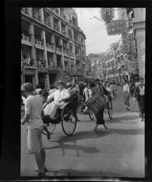 Busy street scene, Hong Kong, including a man in a white suit riding in a hand drawn rickshaw