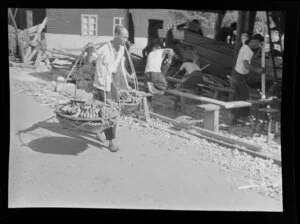 An unidentified Chinese man carries bananas to market using baskets and a shoulder yoke, Hong Kong