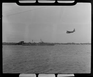 HMNZS Bellona at the 100th Anniversary Day regatta, Auckland Harbour, with a seaplane flying overhead