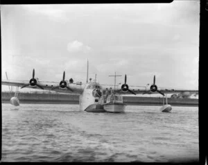 Royal Air Force Sunderland seaplane with a boat drawn up beside it, Mechanics Bay, Auckland