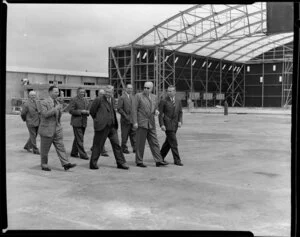 British Overseas Airways Corporation and Tasman Empire Airways Limited employees employees, including (front left to right) Mr Banker, Mr Barrow and Sir Miles Thomas (chairman BOAC) and (second from left at back) Sir Leonard Isitt (chairman TEAL), on the tarmac at an unidentified airport [Mangere?] with hangar being constructed in the background