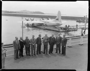 British Overseas Airways Corporation and Tasman Empire Airways Limited employees including (from fourth left) Mr Banker, Sir Leonard Isitt (chairman TEAL), Sir Miles Thomas (chairman BOAC), and Mr Barrow, at Auckland flying boat base, with Short Solent flying boat RMA Ararangi (ZK-AMM) in background