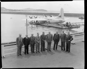 British Overseas Airways Corporation and Tasman Empire Airways Limited employees, including (from fourth left) Mr Banker, Sir Leonard Isitt (chairman TEAL), Sir Miles Thomas (chairman BOAC), and Mr Barrow, at Auckland flying boat base, with Short Solent flying boat RMA Ararangi (ZK-AMM) in background
