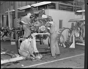 Three unidentified mechanics working on an engine, Tasman Empire Airways Ltd workshop, Mechanics Bay, Auckland